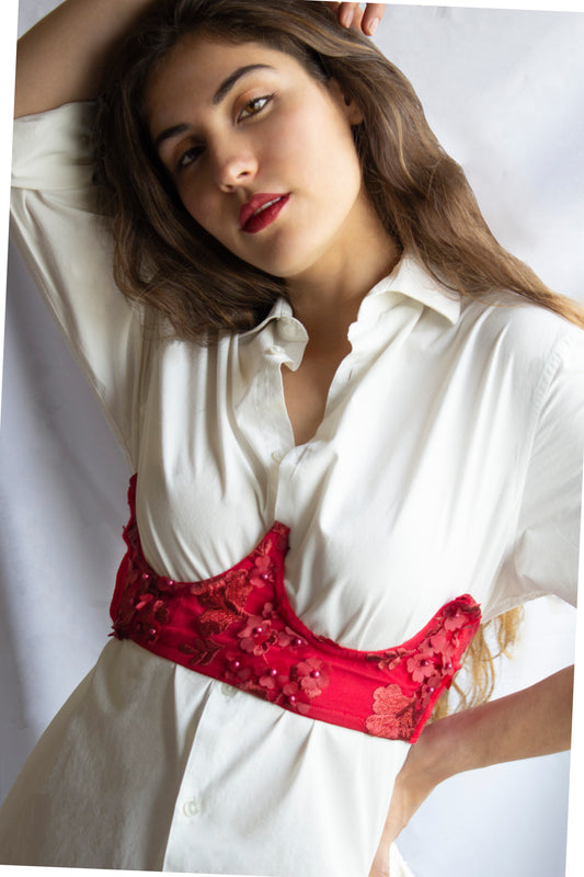 Mujer usando una camisa de botones blanca y un corset sin copas rojo.